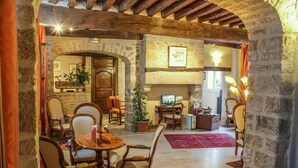 Un intérieur chaleureux et rustique, avec des murs en pierre, des poutres en bois, une cheminée et un coin repas comprenant des chaises et une table.