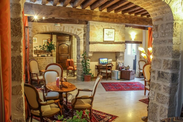 A cozy, rustic interior with stone walls, wooden beams, a fireplace, and a dining area with chairs and a table.