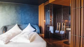 Quarto de hotel moderno com uma cama grande, área de chuveiro envidraçada e painel de parede de madeira.