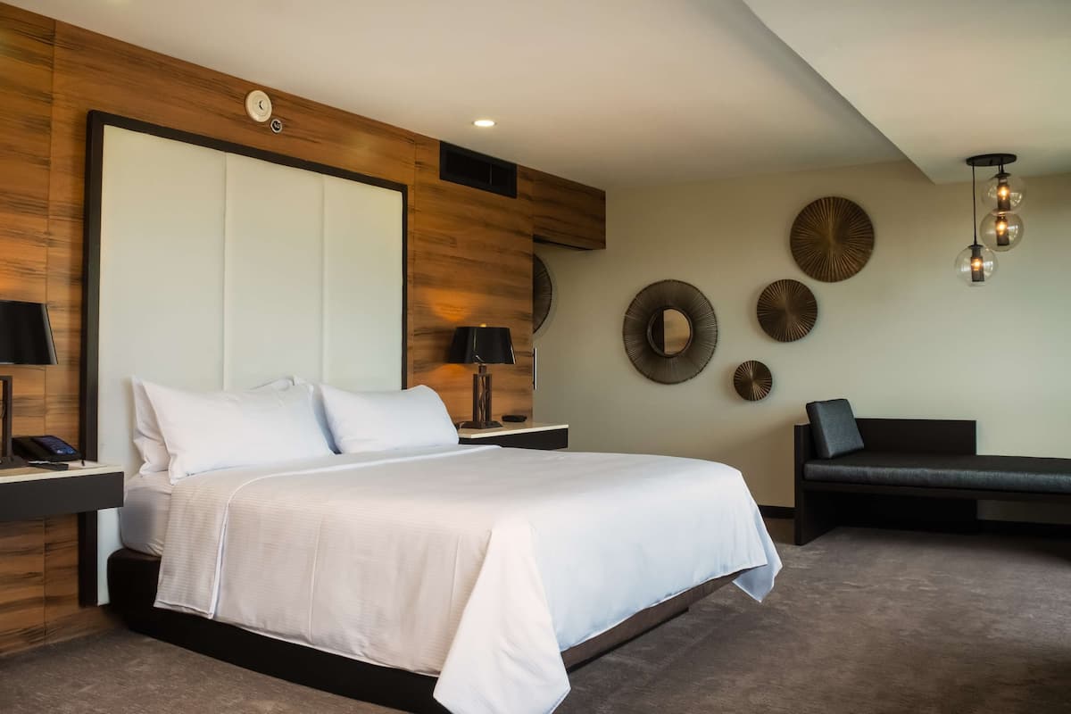 A modern hotel room with a large bed, bedside tables, a wall clock, and decorative wall art.