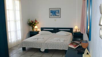 Quarto de hotel com uma cama, duas mesas de cabeceira, um criado-mudo, um vaso com flores, um quadro na parede e um livro no criado-mudo.
