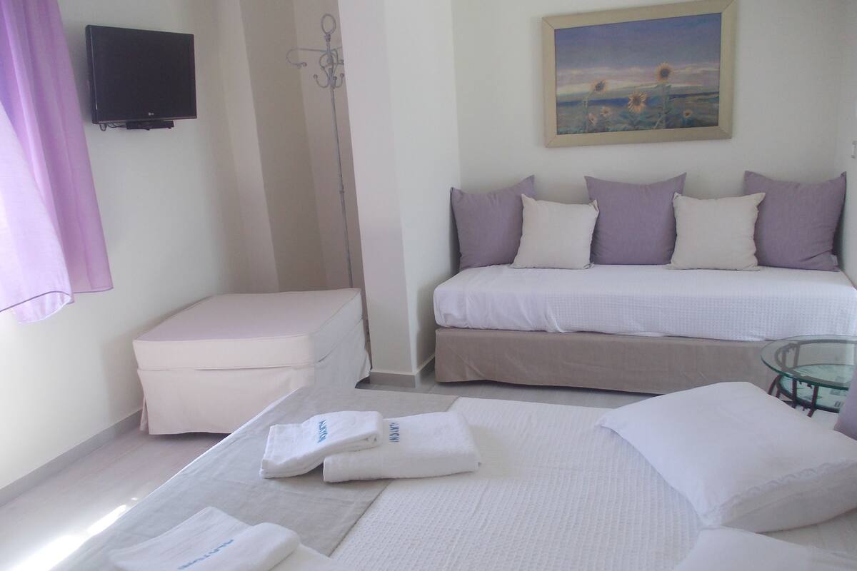 A bedroom with a bed, a small table, a bench, and a painting on the wall.
