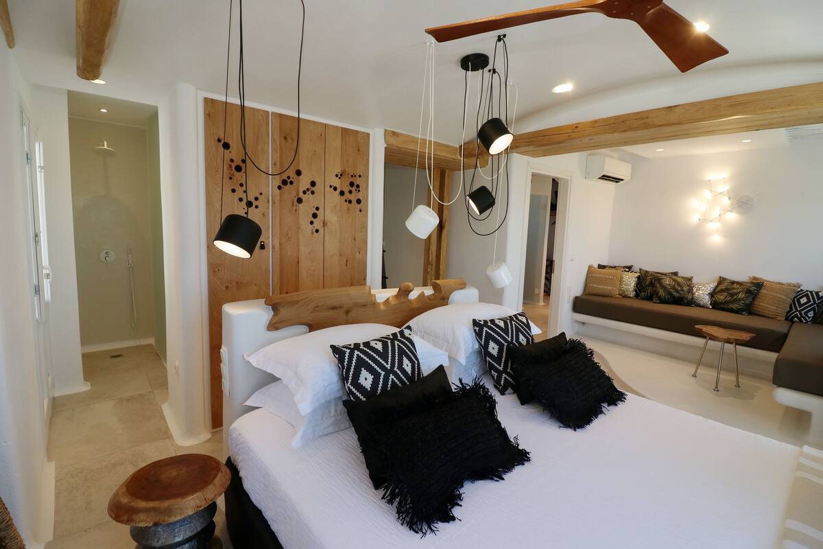 A modern bedroom with a large bed, wooden beams, a wooden wall with circular patterns, a white sofa, and a small wooden stool.