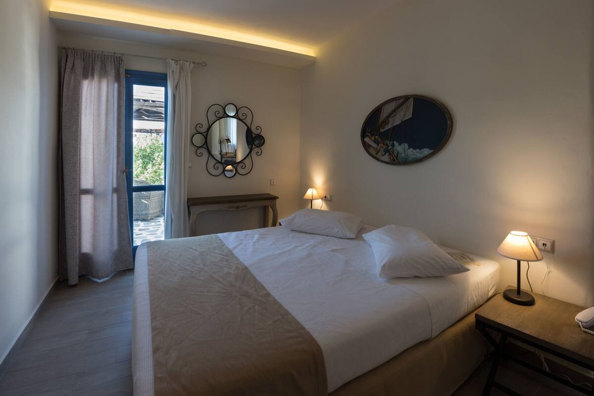 A hotel room with a bed, bedside lamps, a nightstand, a mirror, and a painting on the wall.