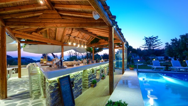 Un área de bar al aire libre con paredes de piedra, una piscina y sillones de descanso.