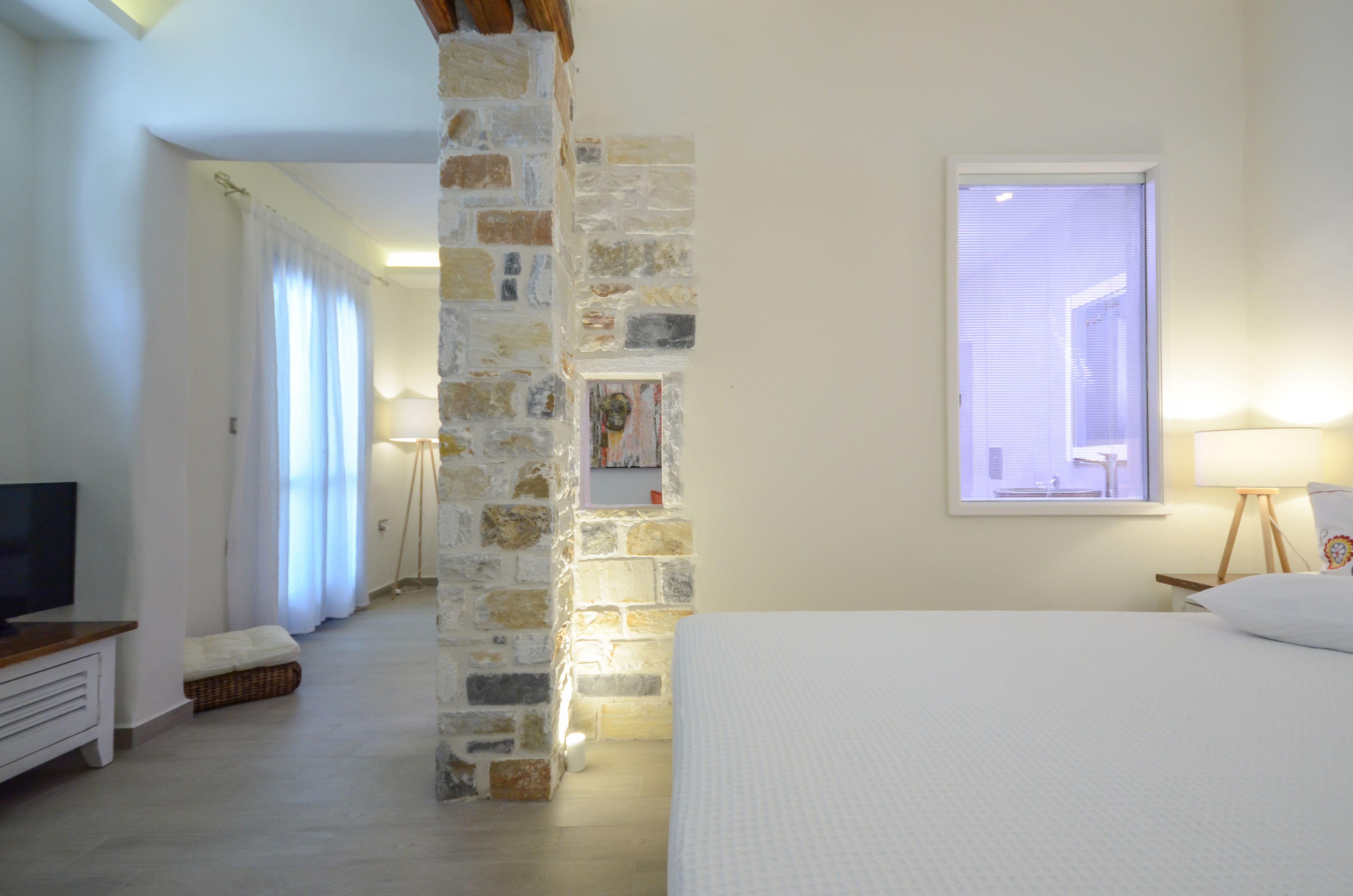 Un dormitorio con pared de piedra, cama, televisor y ventana con vistas.