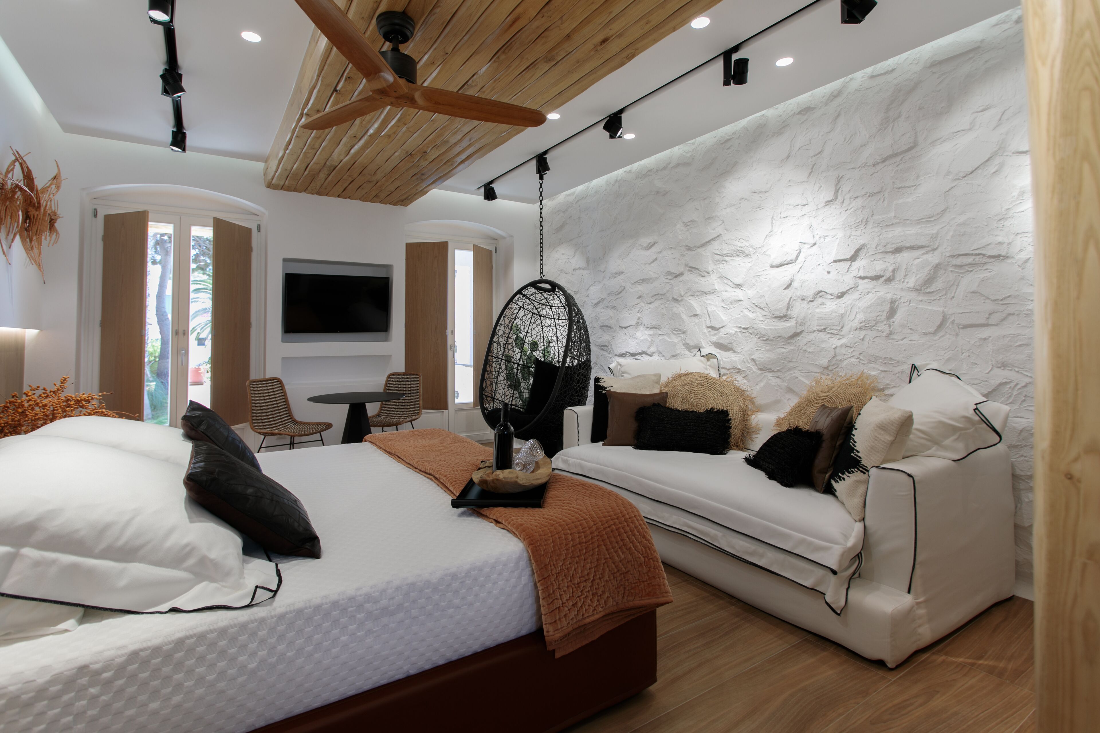 A modern bedroom with a large bed, a sofa, a TV, and a stone-textured wall.