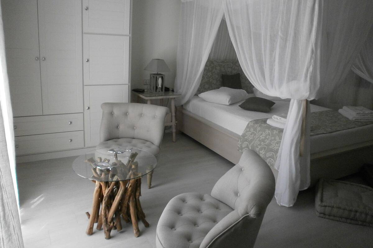 A bedroom with a bed, two chairs, a bedside table, and a wardrobe.