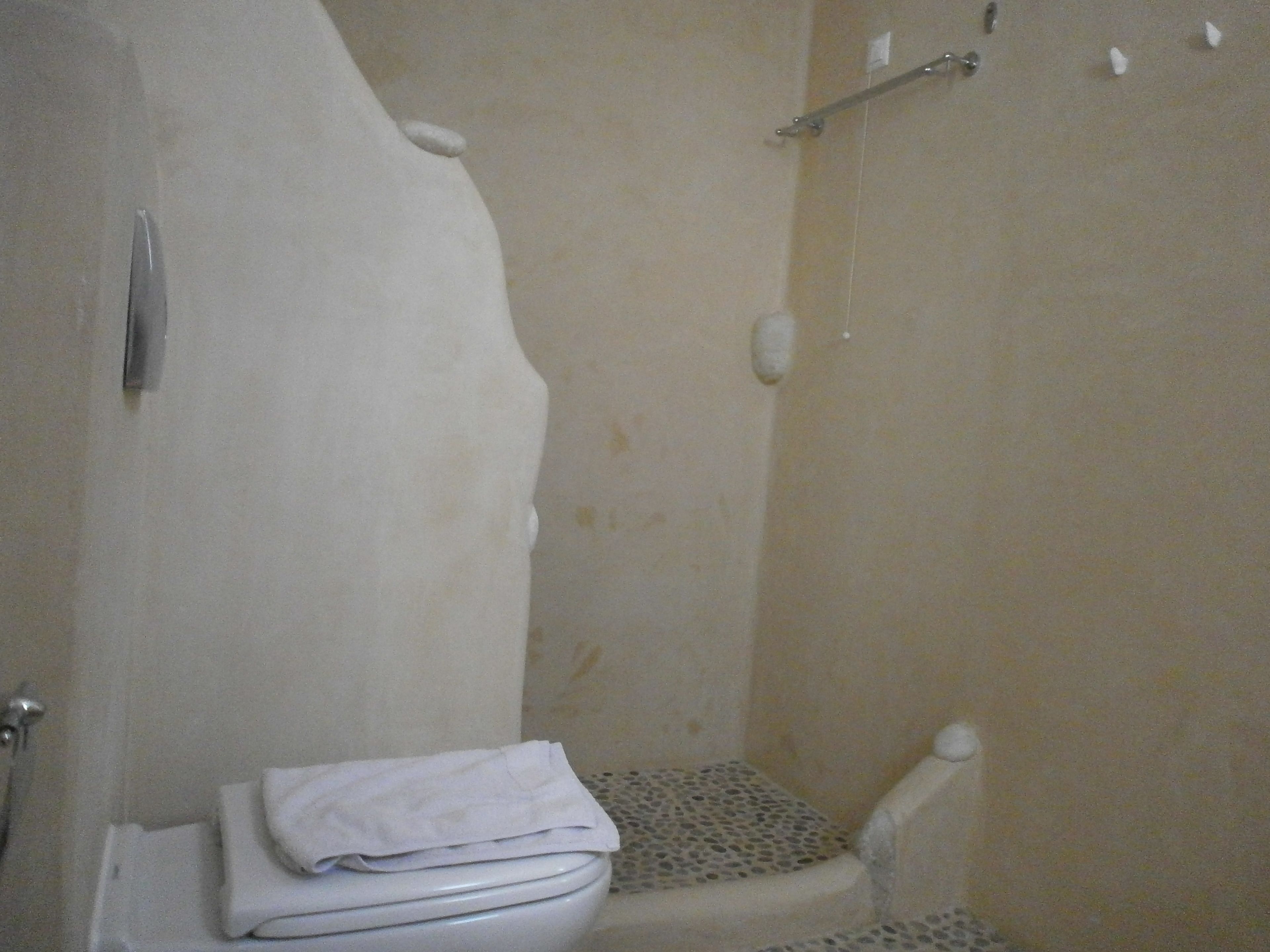 A bathroom with a toilet, a shower area, and a towel placed on the toilet.