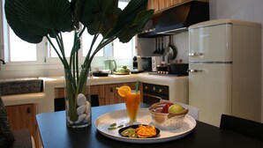 Una cocina moderna con un refrigerador blanco, armarios de madera y una mesa de comedor con un frutero y un vaso de jugo de naranja.