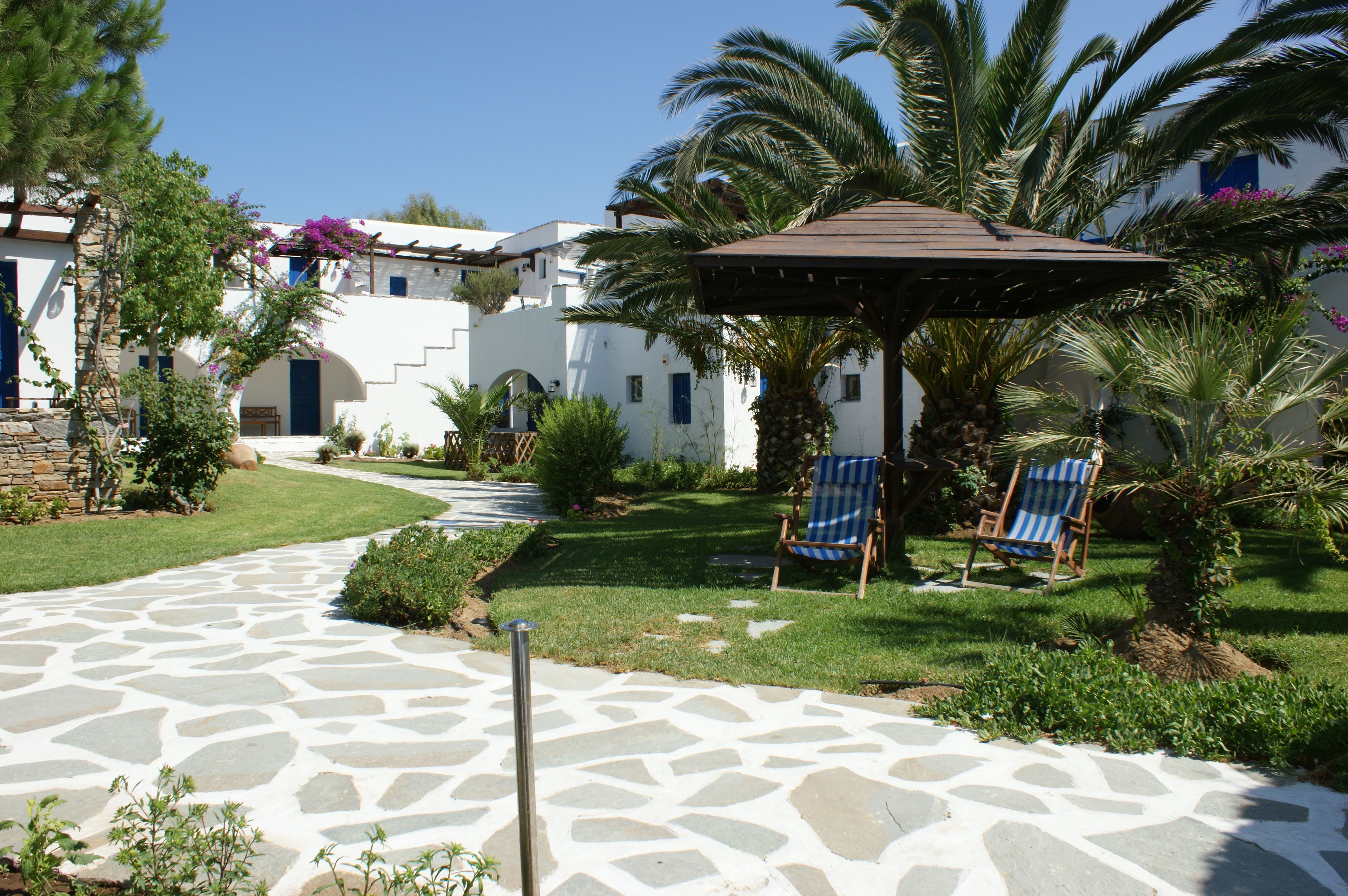 Un patio con un camino de piedra, dos sillas azules, una pérgola y palmeras.