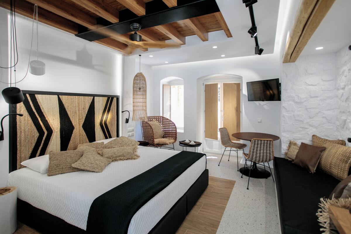A modern bedroom with a large bed, a sofa, a dining table, and a TV.