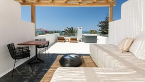 Un balcón con una pérgola de madera, un sofá blanco, una mesa de comedor con sillas y un rincón de lectura con un libro.