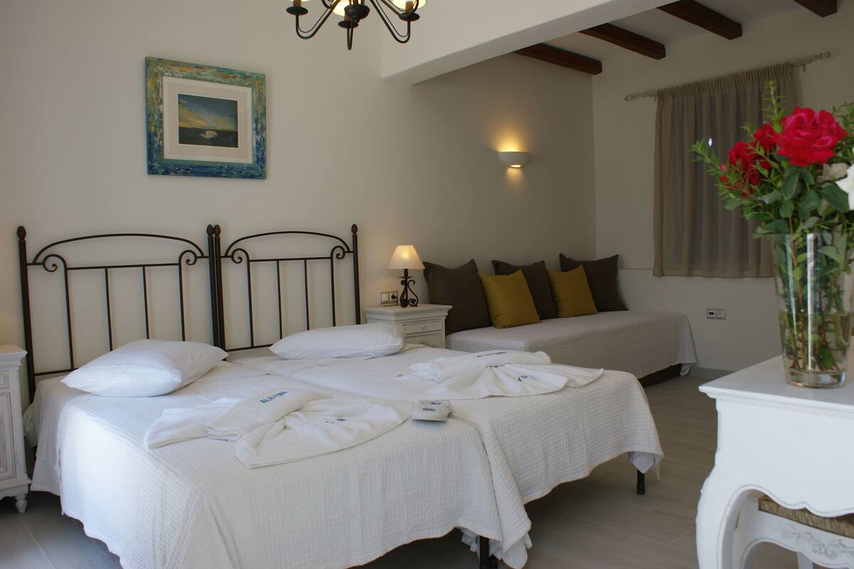 A hotel room with two beds, a nightstand, a bedside table with a lamp, a framed picture on the wall, and a vase with flowers on a table.