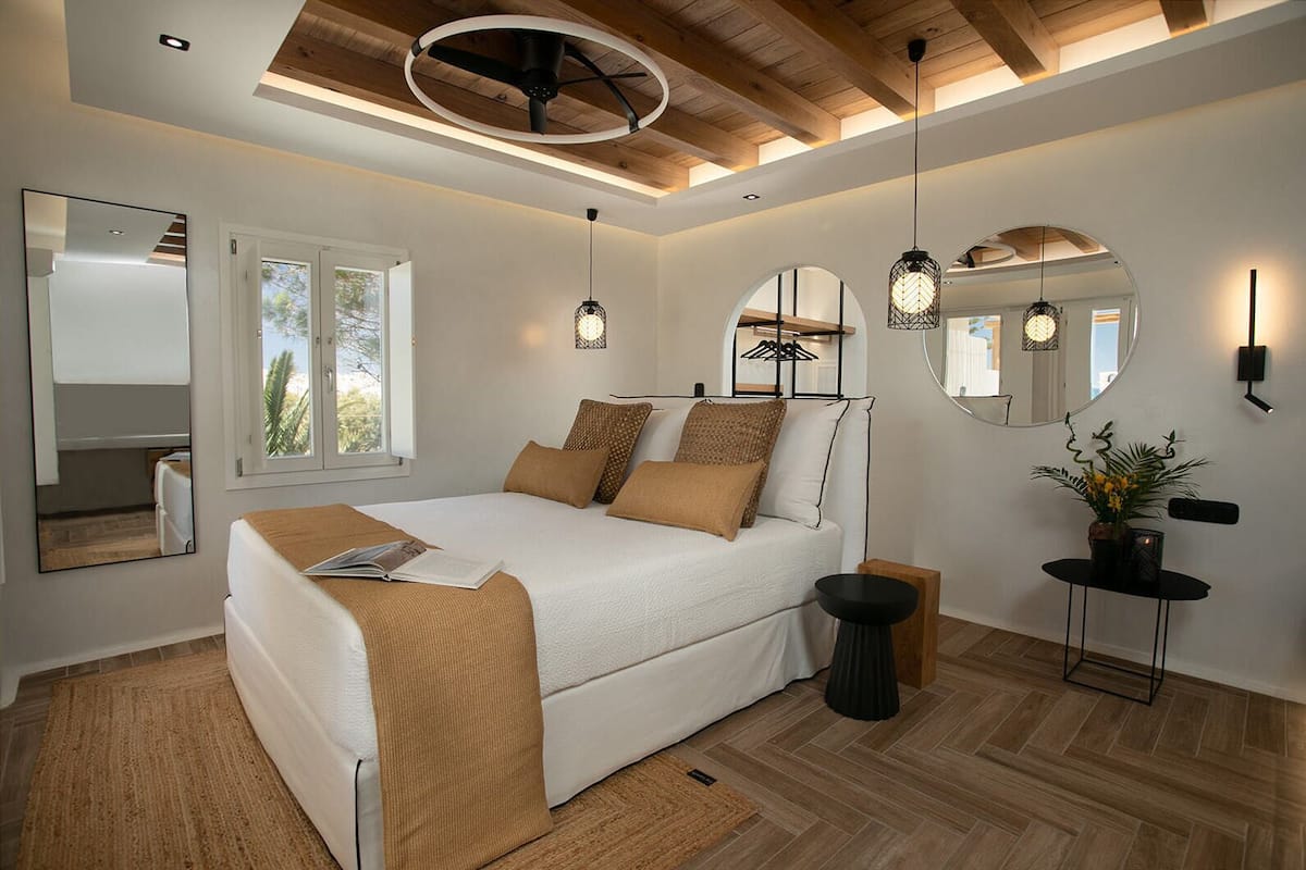 A modern bedroom with a bed, bedside tables, a mirror, and a window.