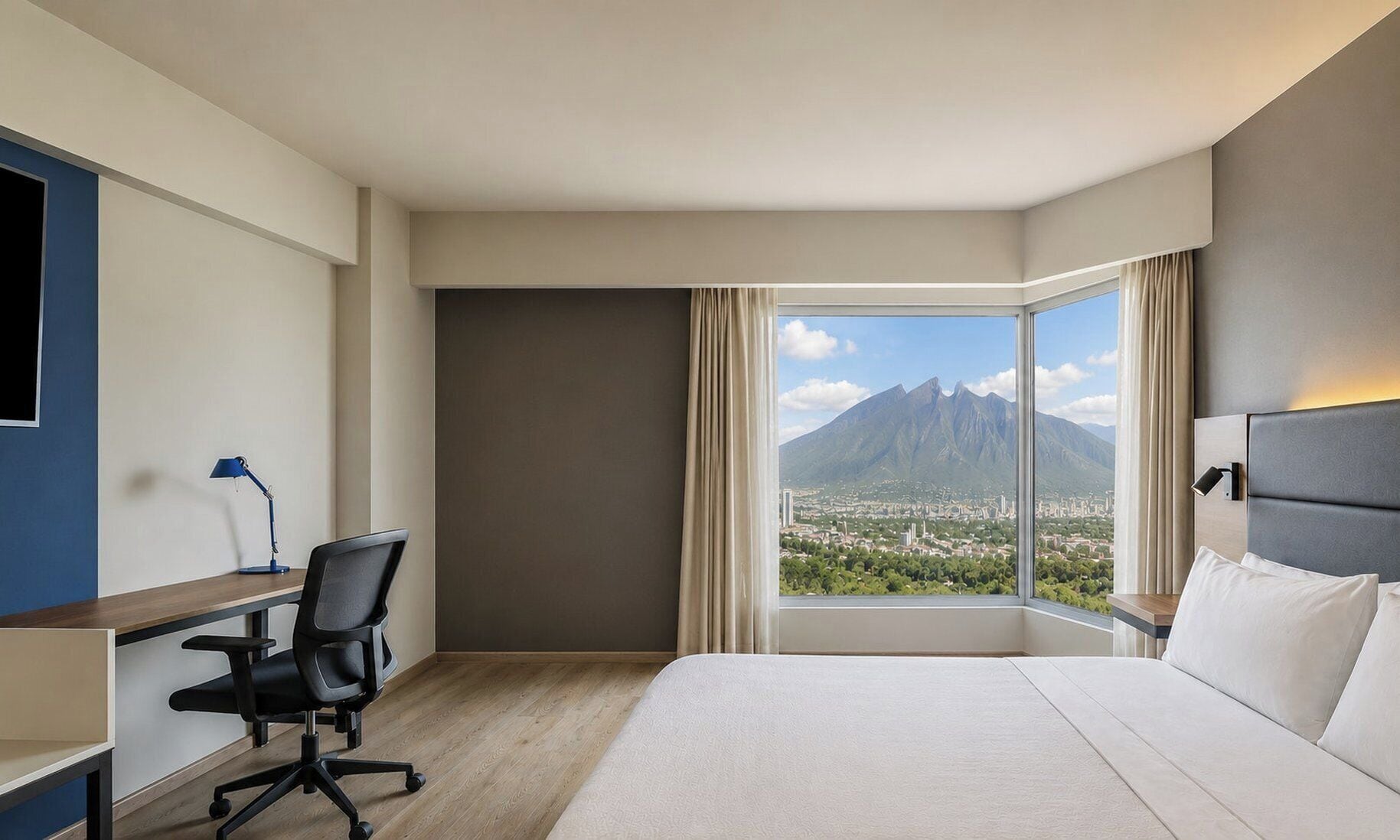 Habitación de hotel con cama, escritorio con silla, lámpara y una ventana grande con vistas a la montaña.