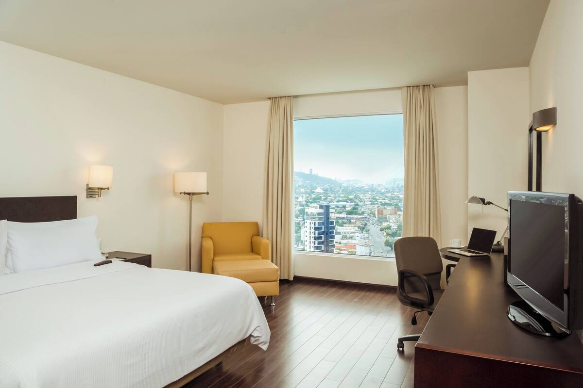 Habitación de hotel con una cama grande, un escritorio con computadora, una silla y un televisor.