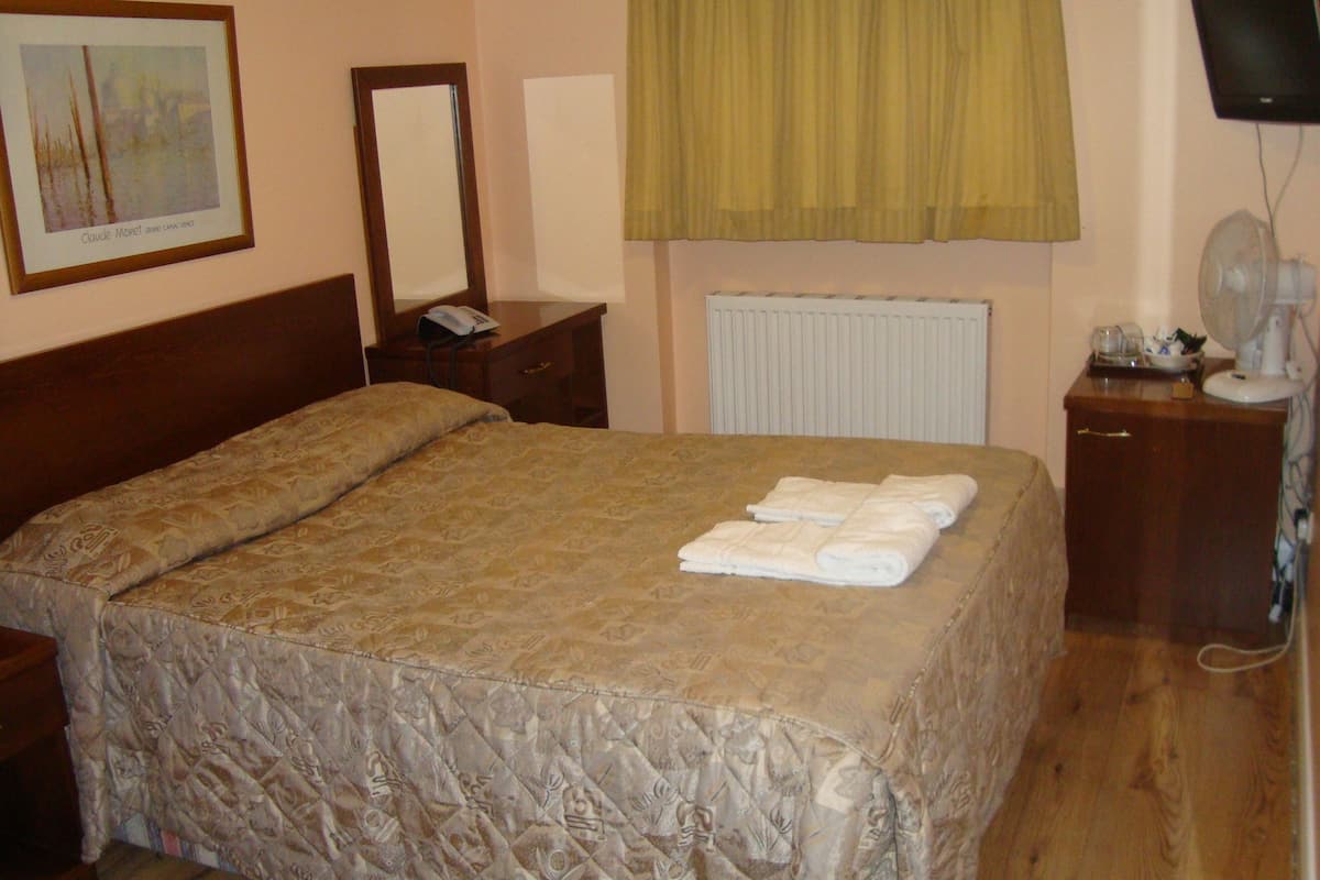 A neatly made bed with a patterned bedspread, a bedside table with a lamp, a mirror, and a framed picture on the wall.