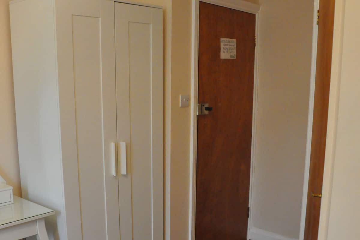 A bedroom with a bed, a wardrobe, a desk, and a door.