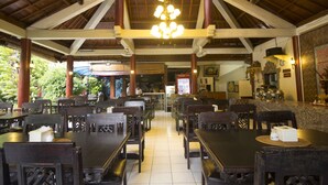 Un restaurante espacioso con techos altos, vigas de madera y un candelabro central. Las mesas están dispuestas en forma de U, y hay un mostrador con un menú y una caja registradora.
