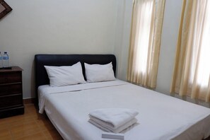Habitación de hotel con una cama, dos almohadas, una mesita de noche con una botella de agua y una toalla doblada.
