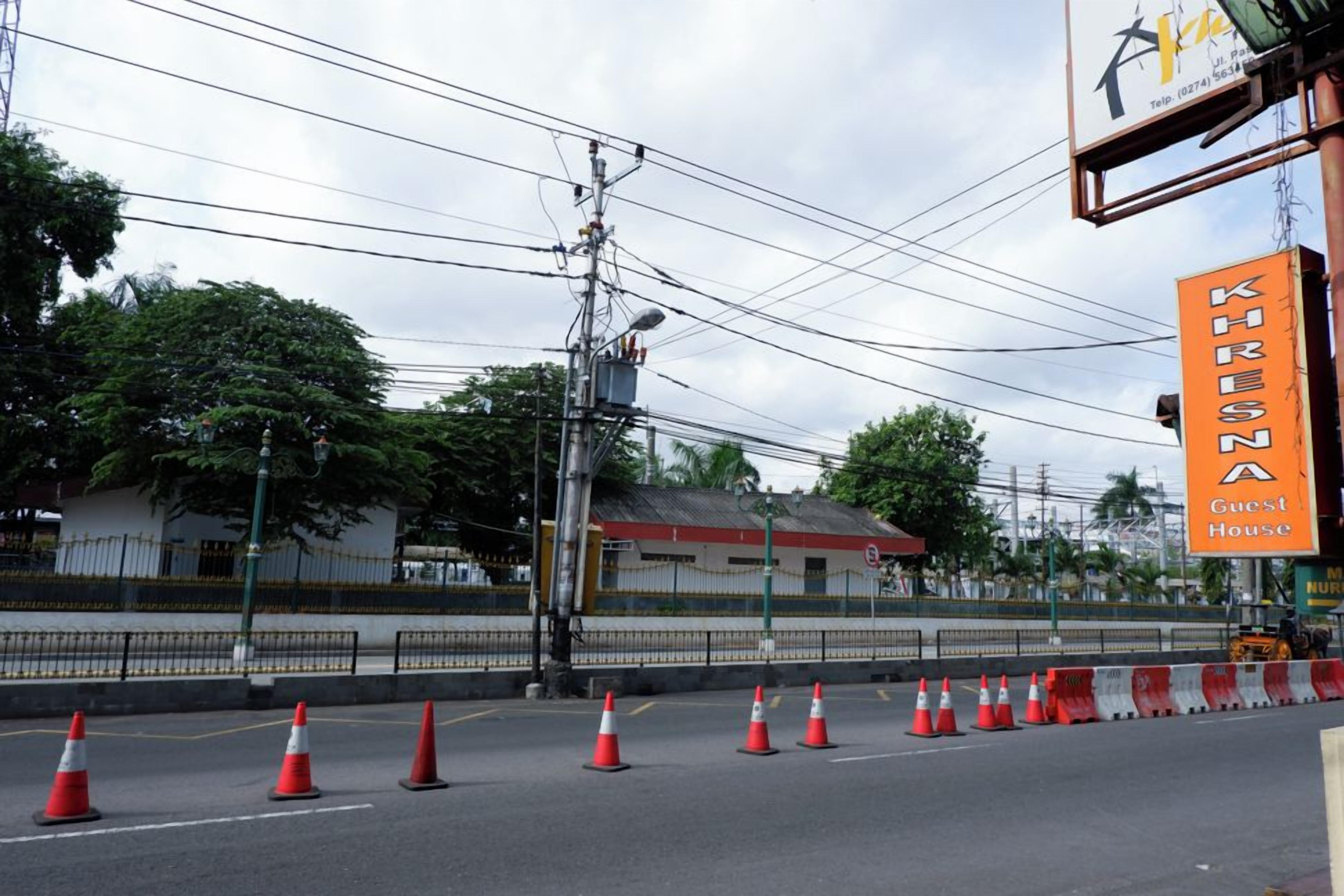 Una carretera con conos de tráfico, un cartel que indica 'KRESNA Guest House' y un poste de electricidad con cables aéreos.