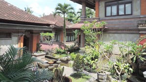 A traditional building with a tiled roof, surrounded by a garden with various plants and a stone pathway. - Nick's Hidden Cottages (Ubud)