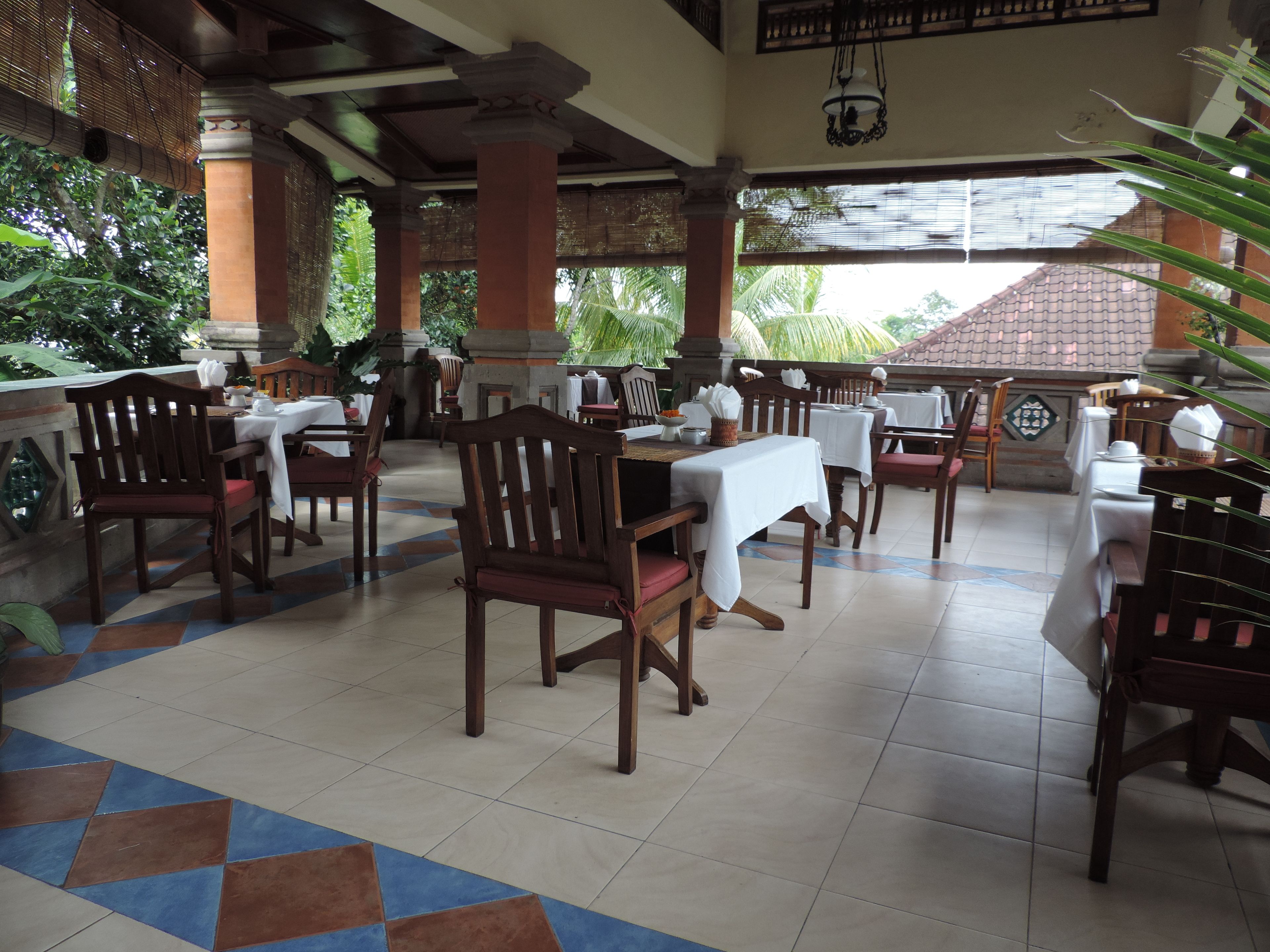 Un restaurante con sillas y mesas de madera, suelo de baldosas y vistas a zonas verdes.