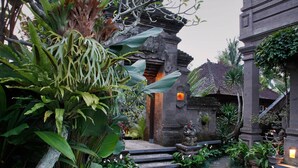 A traditional Balinese temple with stone steps leading to the entrance, surrounded by lush tropical plants and a stone pathway. - Nick's Hidden Cottages (Ubud)