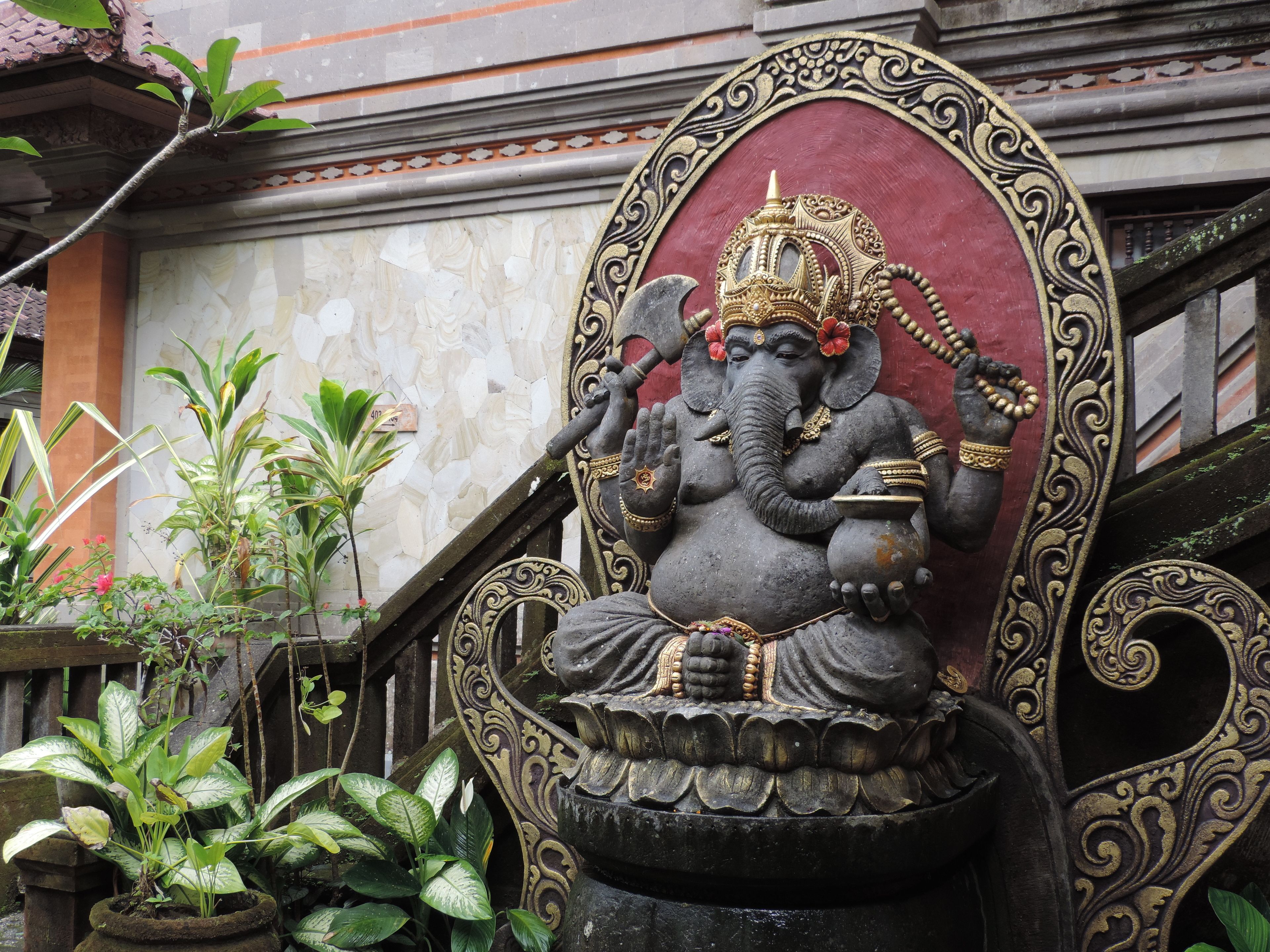 A statue of an elephant deity with ornate decorations, set against a building facade with a tiled pattern and a red background.