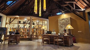 A spacious lobby with a high ceiling and wooden beams, featuring a reception desk, seating area, and a glass storefront displaying various items. - Puri Dajuma Beach Eco-Resort & Spa (Pekutatan)