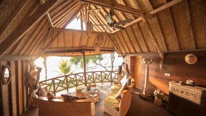 An interior with a high ceiling, wooden beams, wicker furniture, and a view through a balcony. - Puri Dajuma Beach Eco-Resort & Spa (Pekutatan)
