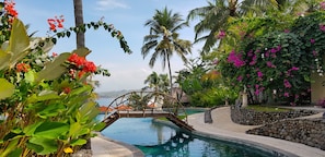 A pool area with a wooden bridge, palm trees, and tropical plants. - Puri Dajuma Beach Eco-Resort & Spa (Pekutatan)