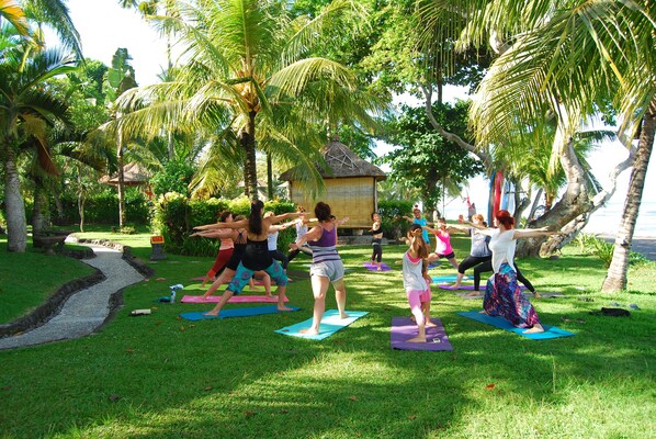 A group of people doing yoga on mats in a grassy area with palm trees and a small hut in the background. - Puri Dajuma Beach Eco-Resort & Spa (Pekutatan)