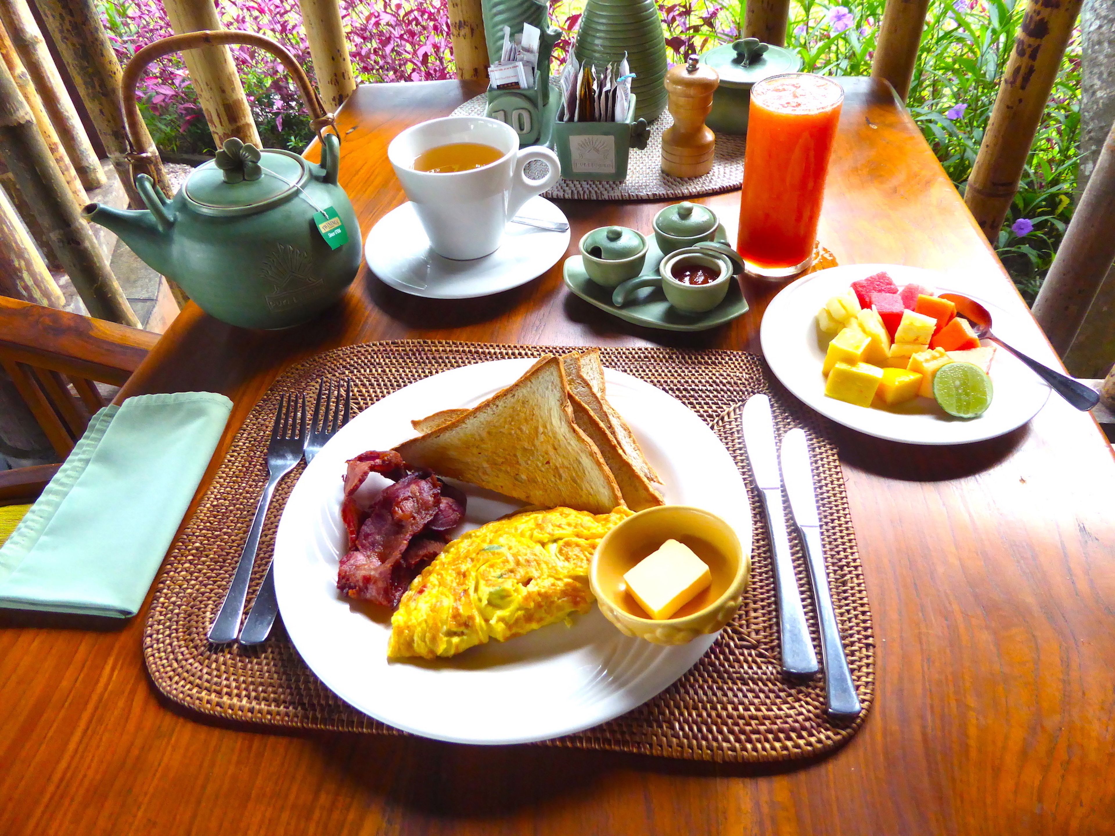 A breakfast table with a plate of toast, bacon, eggs, butter, and a glass of orange juice.