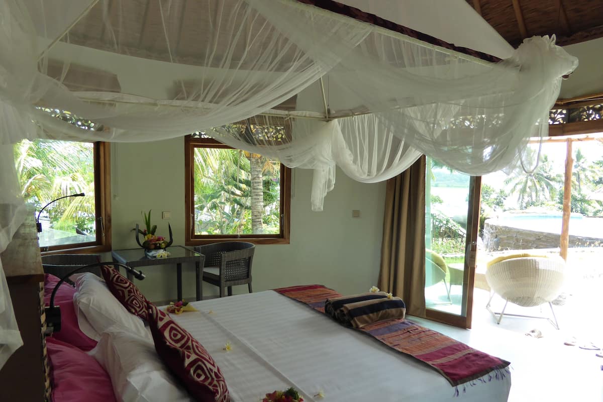 Une chambre à coucher avec un lit, un bureau et une chaise. Il y a des fenêtres donnant sur un paysage verdoyant.