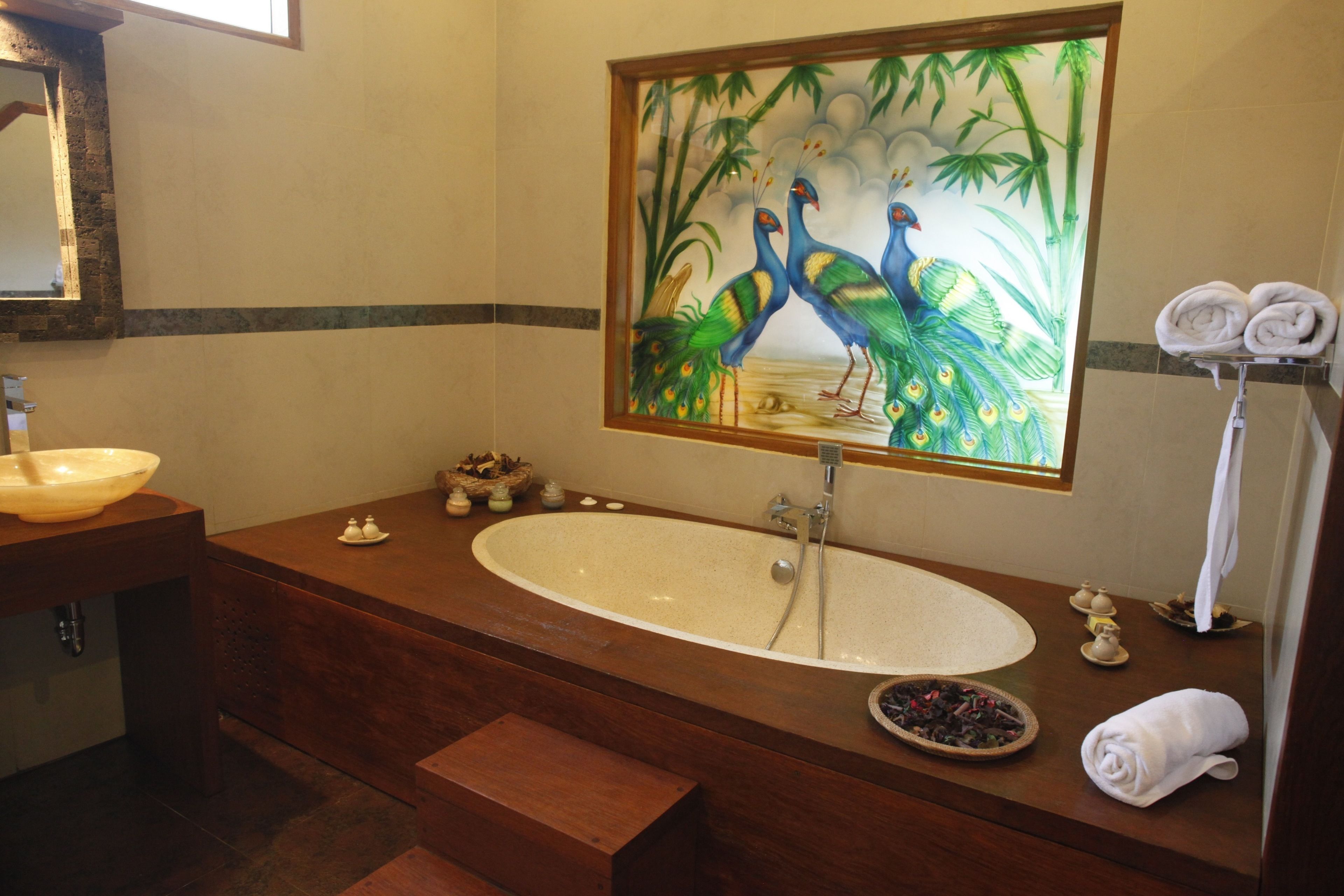 A bathroom with a large oval sink, a wooden vanity, a peacock painting above the mirror, and a towel rack with folded towels.