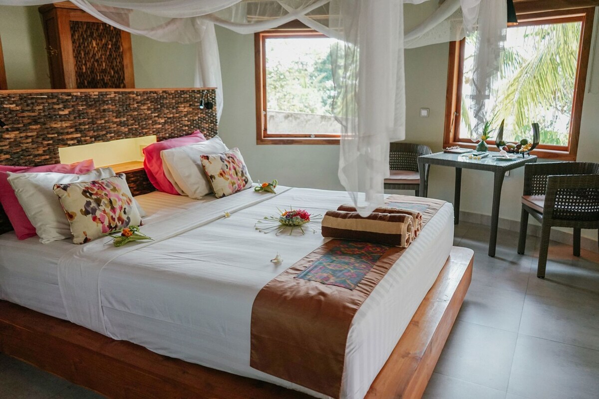A bed with a canopy, a small table with a vase, and a chair.