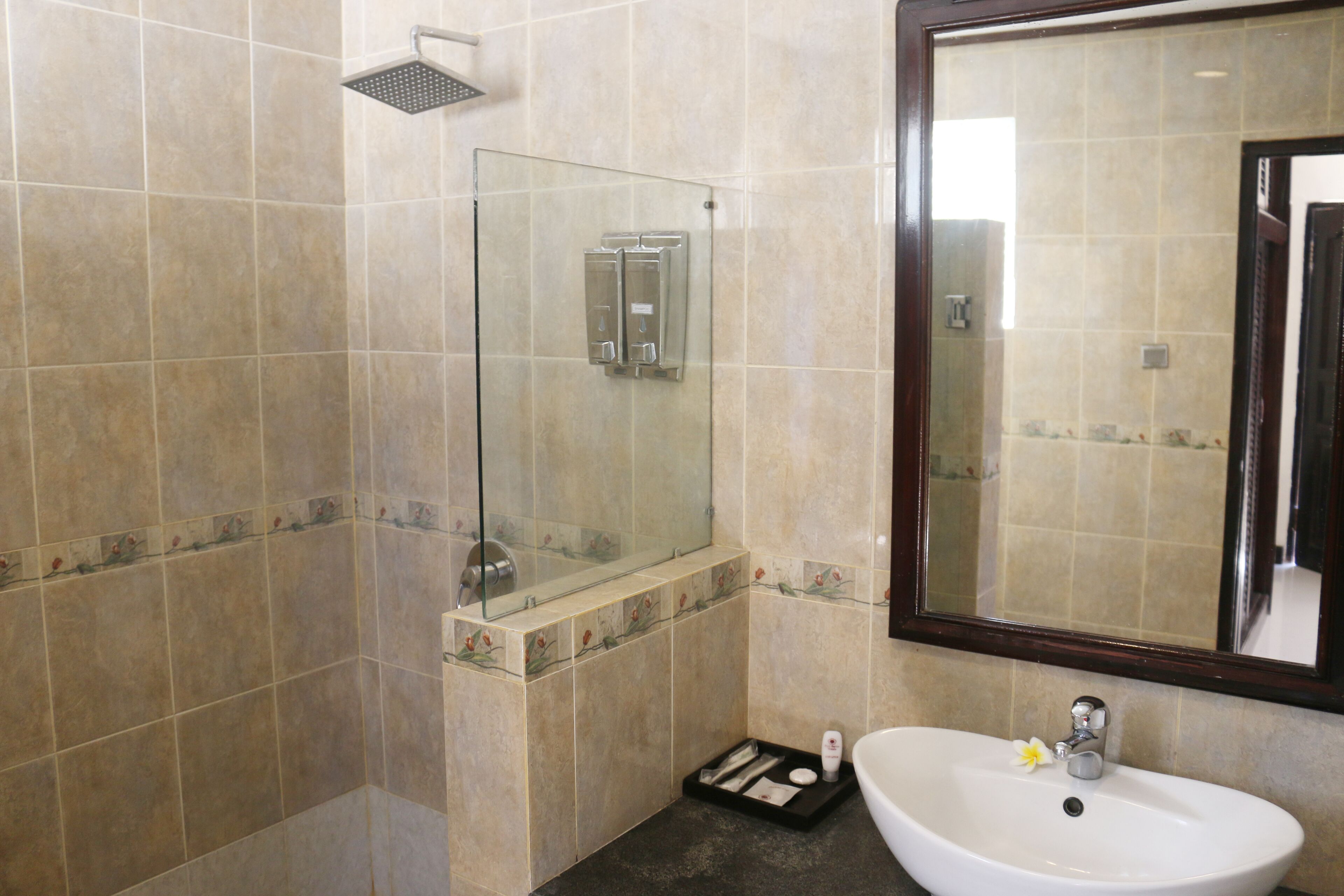 Une salle de bain avec une douche à parois de verre, un lavabo avec un miroir et un petit plateau contenant des articles de toilette.