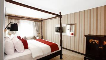 A four-poster bed with a red and white bedspread, a television mounted on the wall, and a dark wooden cabinet.