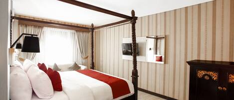A four-poster bed with a red and white bedspread, a television mounted on the wall, and a dark wooden cabinet.