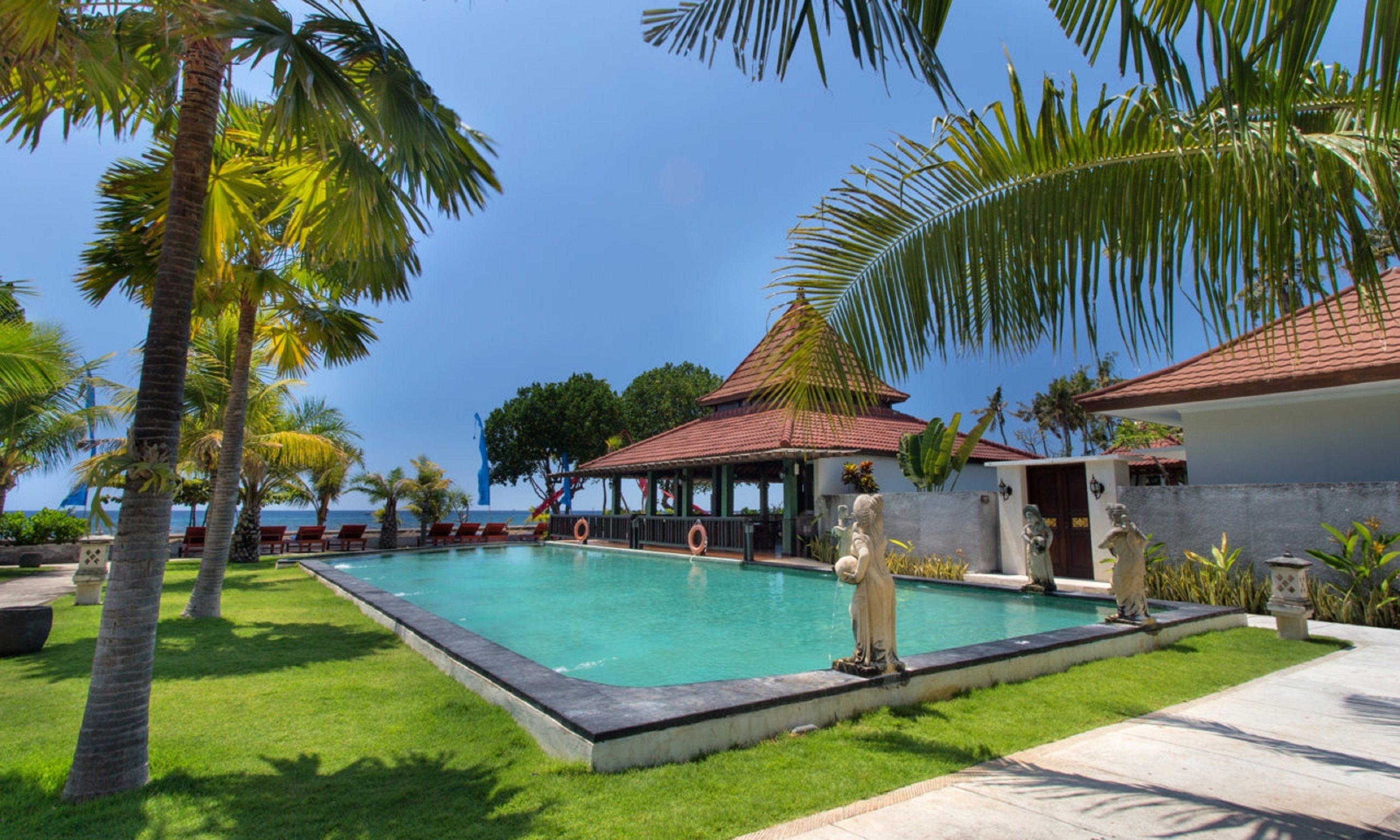 A pool area with a statue, palm trees, and a building with a red roof.