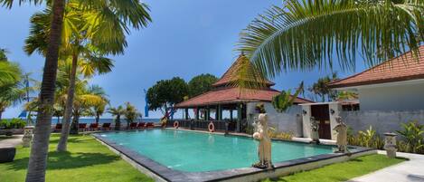 A pool area with a statue, palm trees, and a building with a red roof.