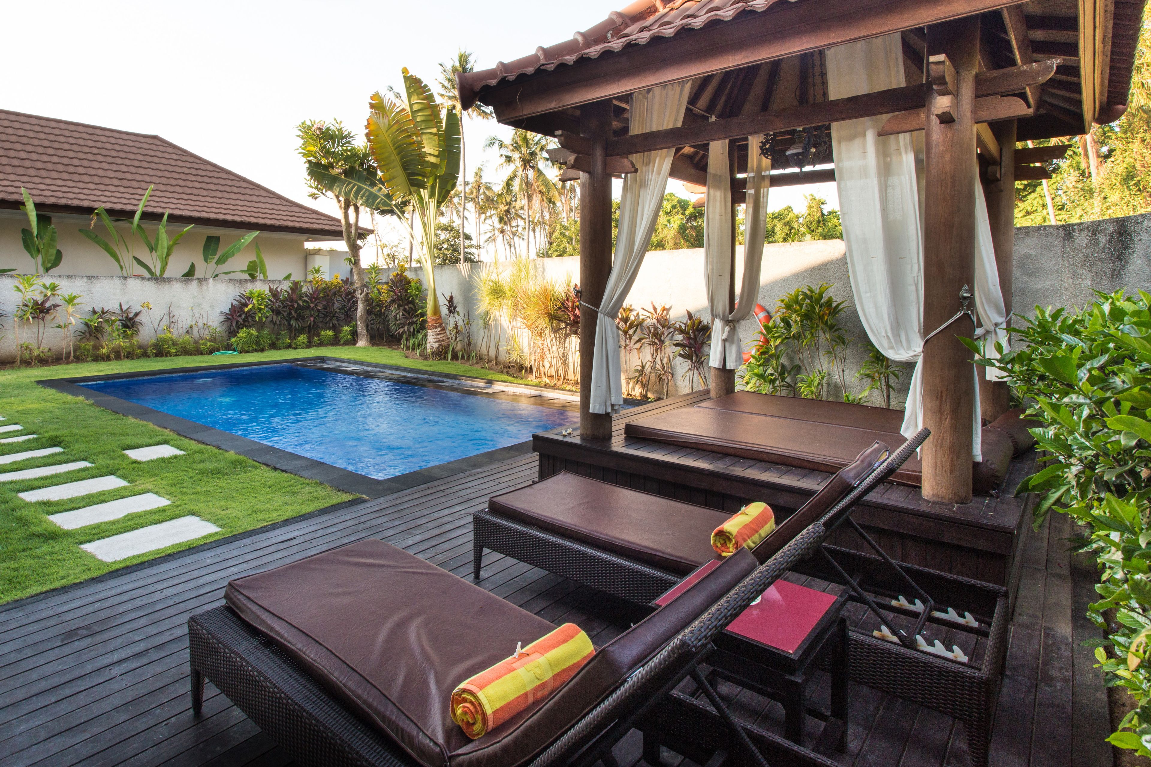 A poolside area with lounge chairs, a wooden deck, and a pergola.