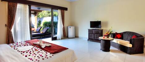 A hotel room with a bed, a sofa, a television, and a minibar.