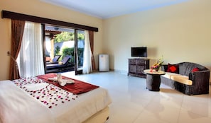 A hotel room with a bed, a sofa, a television, and a minibar.