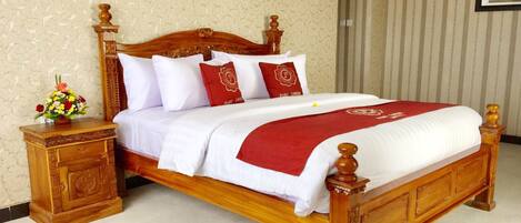 A wooden four-poster bed with white and red bedding, a nightstand with a vase of flowers, and a striped wallpapered wall.
