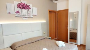 A bedroom with a large bed, bedside tables, a wardrobe, and a mirror. - Monica (Rimini)