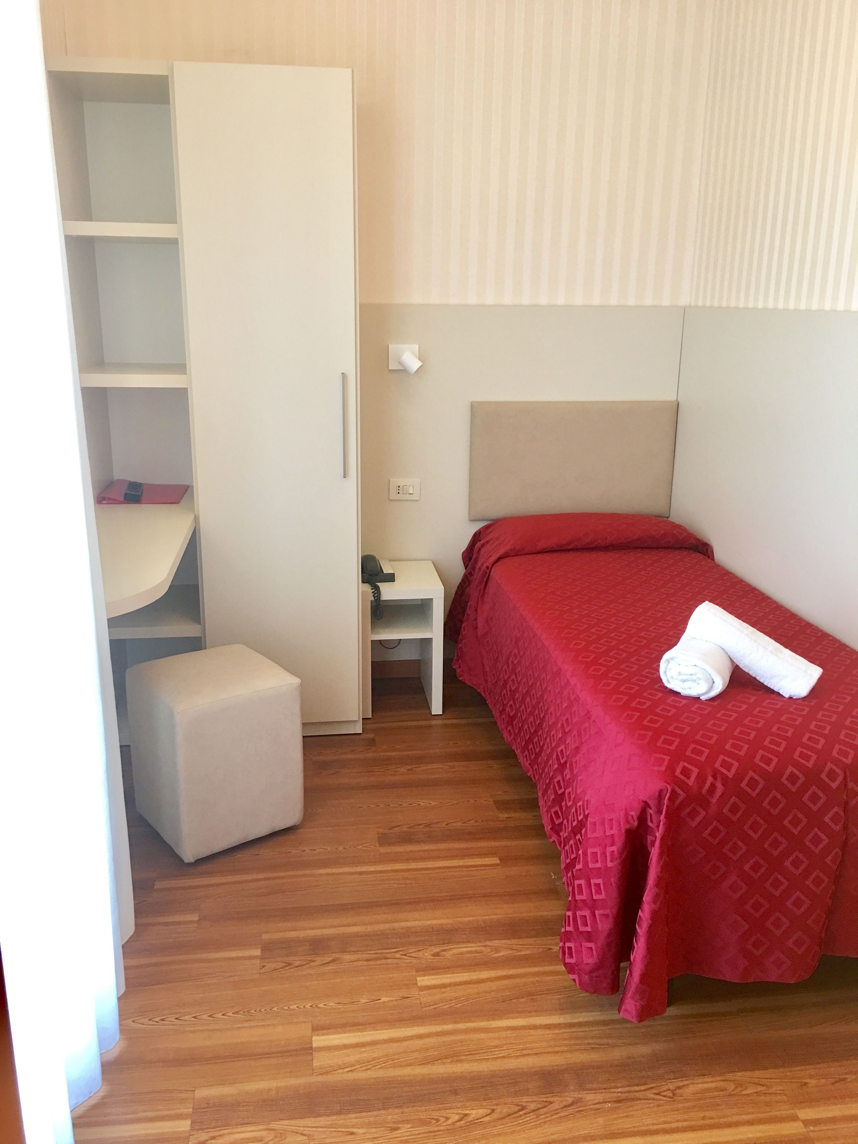 A bedroom with a bed, a nightstand, a wardrobe, and a small stool.