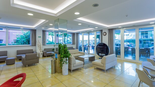 A modern hotel lobby with sofas, a coffee table, and a large mirror. - Monica (Rimini)